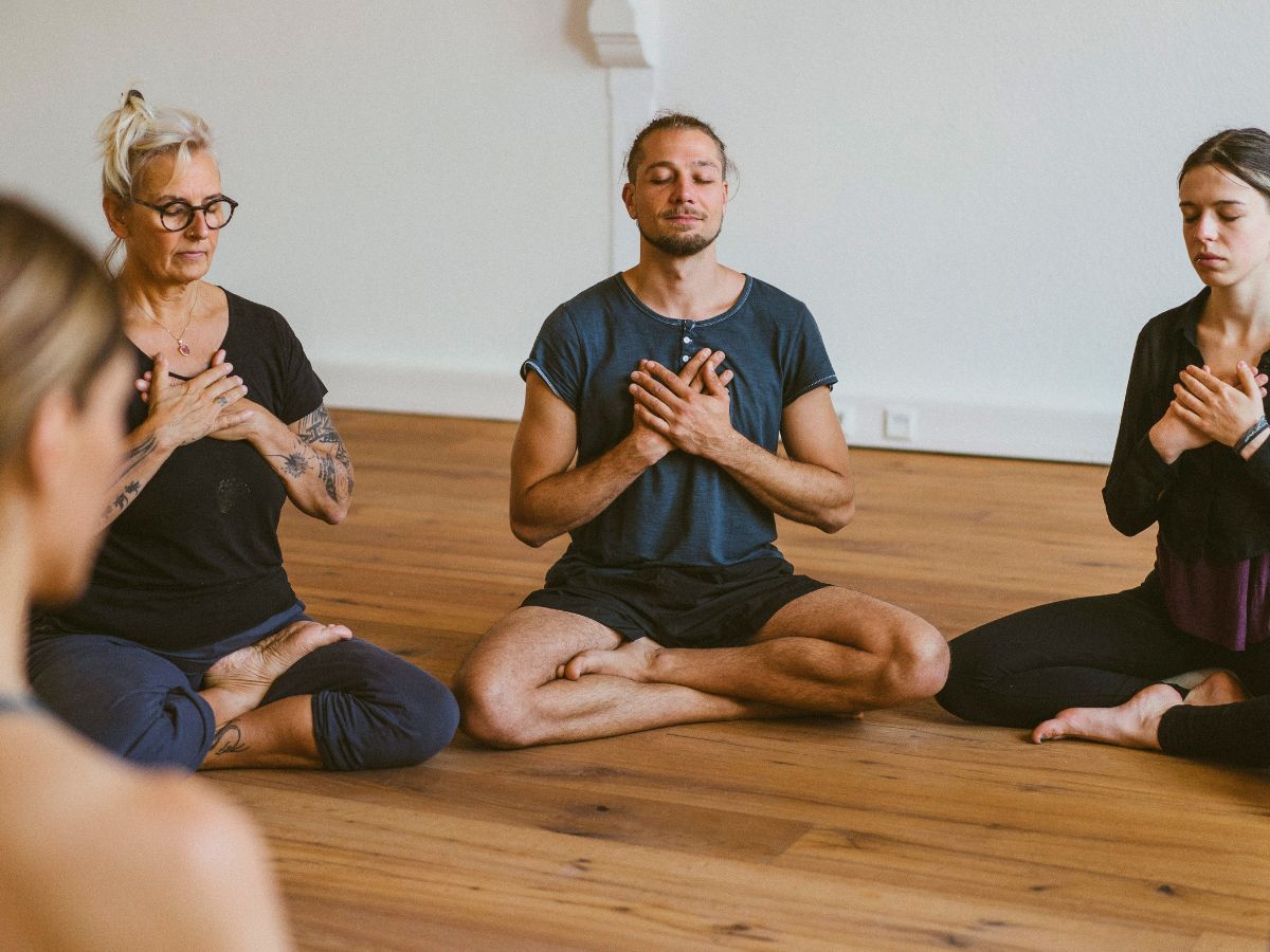 enschen sitzen in stiller Meditation im Kreis mit geschlossenen Augen und Händen auf dem Herzen – achtsame Meditationspraxis beim Sacred Sunday in Lüneburg
